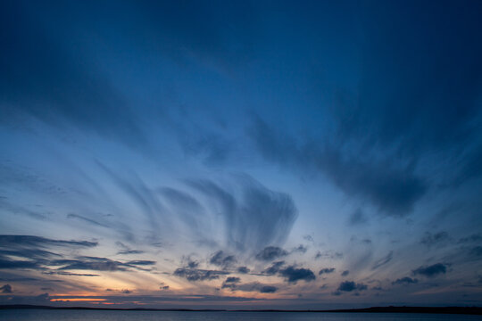 Dark cirrus clouds in a dark blue sky over the first light of sunrise over the North Sea off the East Yorkshire coastline, England, UK