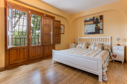 Bright bedroom with large wooden windows, white bed frame, and colorful patchwork bedding
