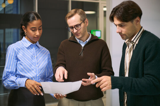 Multiethnic group of young adult business professionals discussing project details while reviewing documents in modern office setting, collaborating and sharing ideas together - Powered by Adobe