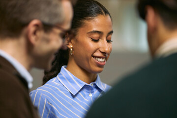 Young adult Black woman smiling while interacting with two colleagues during business meeting, standing in office environment, engaging in professional conversation, teamwork concept