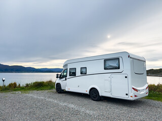 White camper van parked near a tranquil lake and mountains, offering a serene escape for travel and leisure