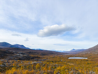 Motorhome driving on a scenic road in Kiruna, Sweden, with autumn foliage and beautiful lake views.