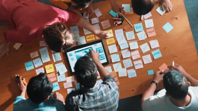 Top down view of programmer brainstorming and planning about web design while looking at tablet wireframe prototype. Aerial view of skilled developer team talking about digital application. Symposium.
