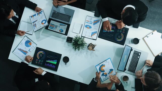 Top down aerial view of business people discussing about financial strategy on table with document and tablet display investment statistic at meeting. Diverse team brainstorm about plan. Directorate.