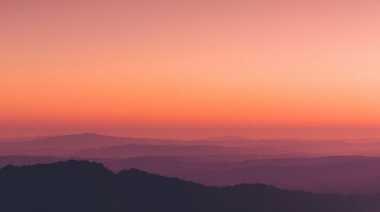Fototapeta premium Vibrant hues of orange and purple blend softly above distant mountains at dusk.