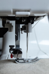 a side view of a sewing machine presser foot on fabric with beige thread visible in the needle