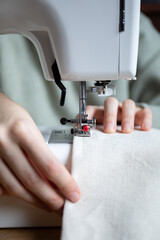 a front view of a woman's hands sewing beige fabric on a sewing machine