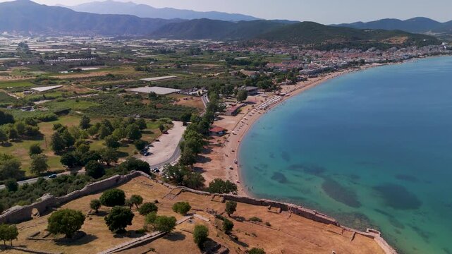 High altitude aerial wide shot soaring over the picturesque coastal town of Nea Peramos, nestled on the Thracian Sea coastline near Kavala, Eastern Macedonia, Greece.