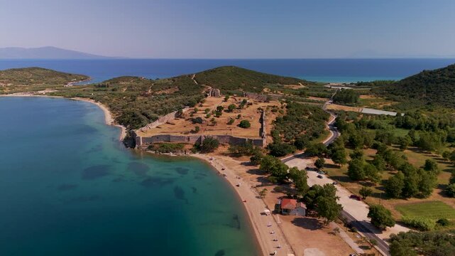 Aerial pan shot revealing the extensive ancient ruins of Anaktoroupolis overlooking the coastal landscape of Nea Peramos, Greece.