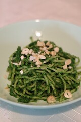 Process of preparing pasta with pesto from spinach, basil, green peas and green parsley: ready dish on a plate, sprinkled with chopped cashew nuts