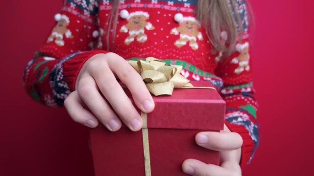 Slow motion closeup of a girl opening a wrapped gift box in front of a festive red background