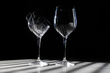 broken wine glass next to a whole one minimalism white background with shadows