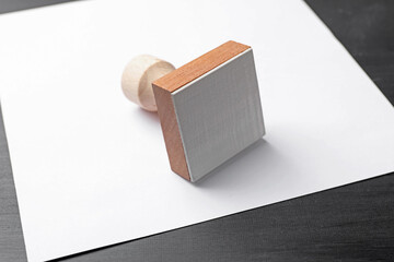 One wooden stamp and blank sheet of paper on black table, closeup. Space for text