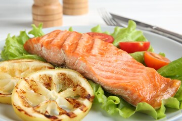 Piece of tasty grilled salmon, lemon slices and salad on white table, closeup