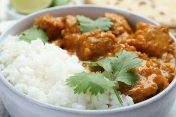 Delicious chicken tikka masala with rice and cilantro in bowl on table, closeup