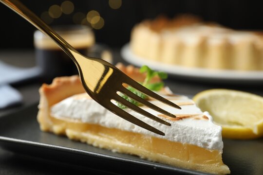 Eating slice of tasty lemon meringue tart with fork on black table, closeup - Powered by Adobe