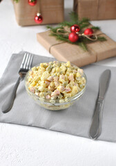A festive bowl of traditional Olivier salad sits on a table with cutlery, surrounded by wrapped gifts and red ornaments, creating a cozy Christmas holiday atmosphere.