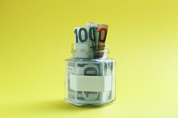 Jar with blank note and money on yellow background