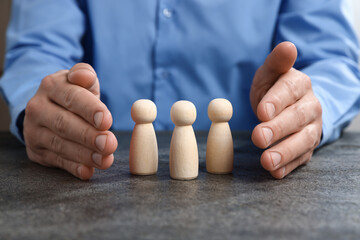 Man protecting human figures at grey table, closeup