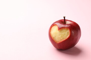 Red apple with carved heart on light pink background, closeup. Space for text