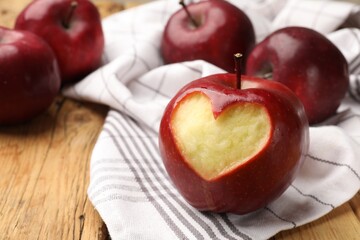 Red apple with carved heart and other fruits on wooden table, closeup