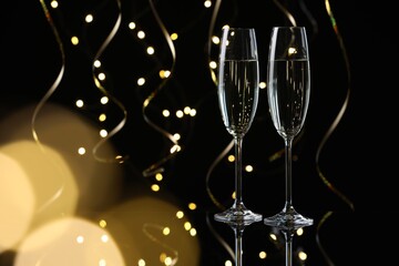 Happy New Year. Sparkling wine in flute glasses and serpentine streamers on black background, bokeh lights