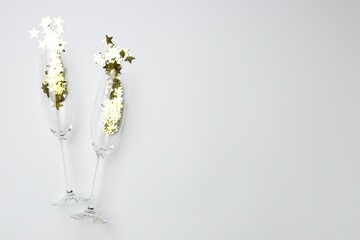 Merry Christmas and Happy New Year. Flute glasses with golden star shaped confetti on white background, flat lay. Space for text