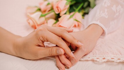 Fototapeta premium Hands of a romantic couple tenderly holding on a pink background, symbolizing connection, love, support, and care, with soft pink roses creating a gentle and intimate atmosphere