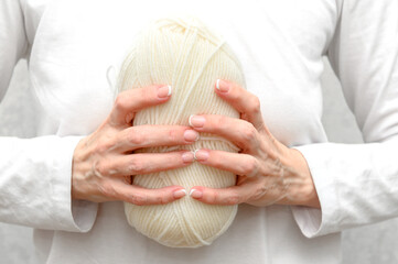 A woman in a white sweater holds beige hand-knitted yarn in her hands.