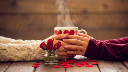 Couple hands holding a steaming heart patterned cup on a rustic wooden table. Expressing warmth. Love. Romance. And togetherness during a cozy date