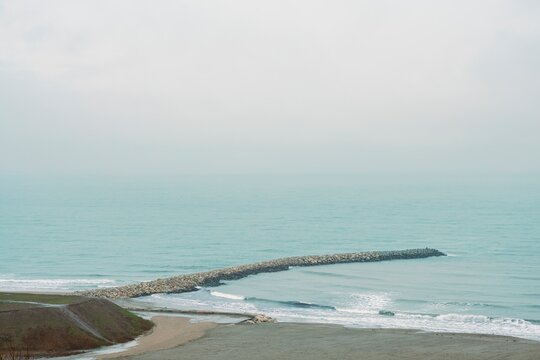 A serene view of a rocky jetty extending into the calm Black Sea, with gentle waves and a soft mist enveloping the coastline of Constanta, Romania. Nature's beauty unfolds in quiet harmony