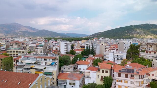 Breathtaking aerial drone rise shot revealing the sprawling city of Drama, Eastern Macedonia, Greece, showcasing urban architecture, rooftops, and roads under an overcast sky.