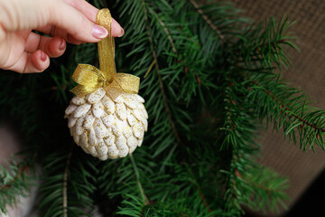 Handmade white ornament with gold ribbon held above fir branches with soft focus and authentic natural look. Concept of eco decoration, holiday design and marketing visuals.