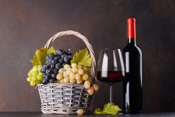 Naklejka premium Red wine bottle with a glass and basket of fresh grapes