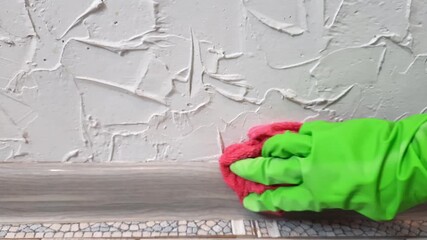 Hand in rubber glove cleaning baseboard with household sponge closeup. gloved hand washing scrubbing wall with household sponge in home or office interior. professional or domestic maintenance.