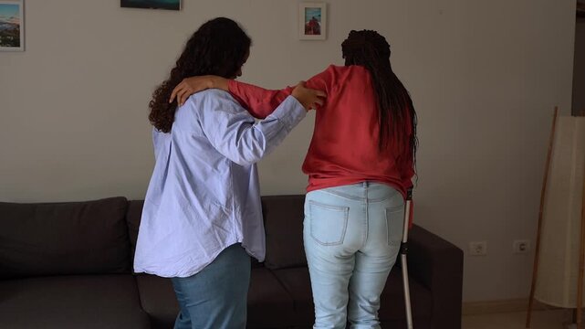 African daughter helping her mother to walk after foot injury - Rehabilitation, health care and family concept 
