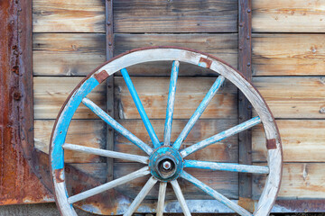 Old wooden wagon wheel leaning on rustic wooden wall.