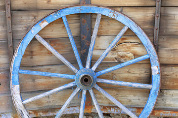 Vintage wooden wagon wheel in front of weathered wooden wall.