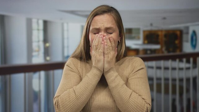 Woman expressing stress and frustration in a modern hotel setting, leaning on a railing with her hands on her face, conveying indoor emotional struggle and tension.