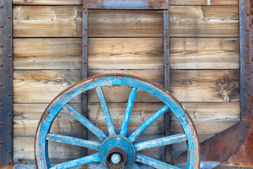 Old wooden wagon wheel leaning on rustic wooden wall.