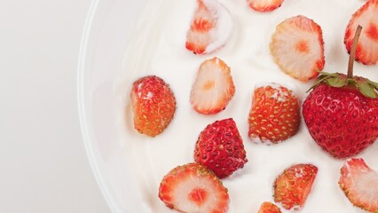 Fresh strawberries in creamy white yogurt, lactic acid product close up top view. Healthy dairy dessert or breakfast with seasonal fruit. Natural nutrition. Lactose free kefir yogurt. Food background