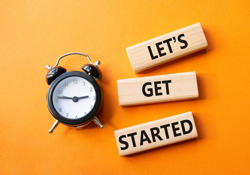 Lets get started symbol. Concept words Lets get started on wooden blocks. Beautiful orange background with alarm clock. Business and Lets get started concept. Copy space.