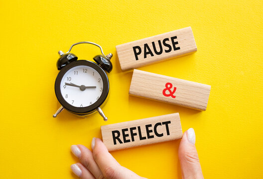 Pause and Reflect symbol. Concept words Pause and Reflect on wooden blocks. Businessman hand. Beautiful yellow background with alarm clock. Business and Pause and Reflect concept. Copy space.