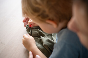 Busy mother working as a tailor at home, unpicking a seam on trousers with her baby sitting on her lap and helping. Top view.