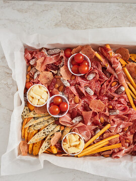 A bountiful platter showcases a variety of cured meats, cheese cubes, cherry tomatoes, and crunchy snacks, perfect for sharing at a festive gathering or casual get-together