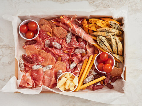 A charcuterie board displays a variety of cured meats, cheeses, cherry tomatoes, breadsticks, and snacks arranged for a lively evening. Perfect for sharing with friends
