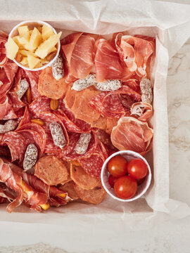 A beautifully arranged platter features a variety of cured meats, cheeses, and nuts, complemented by fresh cherry tomatoes. Perfect for social events or relaxed evenings