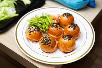 Gourmet sliders with vegetables. A delectable arrangement of gourmet sliders topped with black sesame seeds, accompanied by fresh green beans and lettuce. 