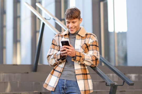 Smiling man in shirt with smartphone near railings outdoors