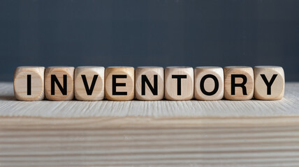 Inventory management concept displayed with wooden blocks spelling inventory on a light wood surface against a dark representing stock and supply chain